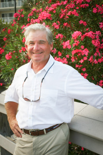 Wayne Raper smiling in a white shirt with pink flowers in the background